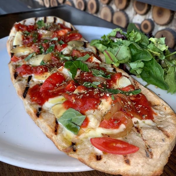 Grilled flatbread with tomato sauce, mozzarella, artichoke hearts, basil, and a side salad.