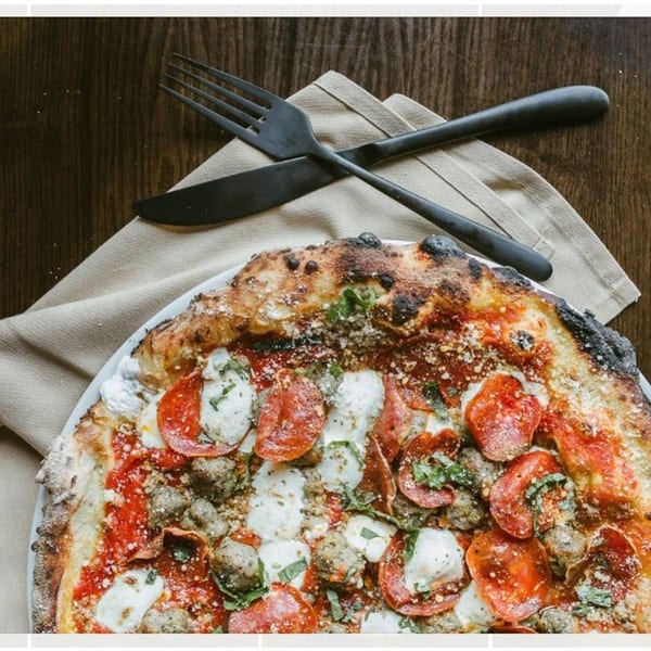 Close-up of a pepperoni, sausage, and fresh mozzarella pizza with a charred crust.