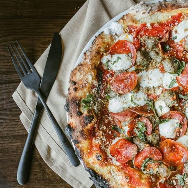 Close-up of a pepperoni, sausage, and mozzarella pizza with basil on a white plate.